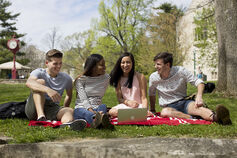 A small group of students on the IU Bloomington campus sitting on a blanket on a beautiful spring day.
